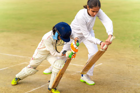 Girl cricketer coach ke saath bat grip adjust karti, helmet pads mein proper stance practice - girls cricket drills amethi